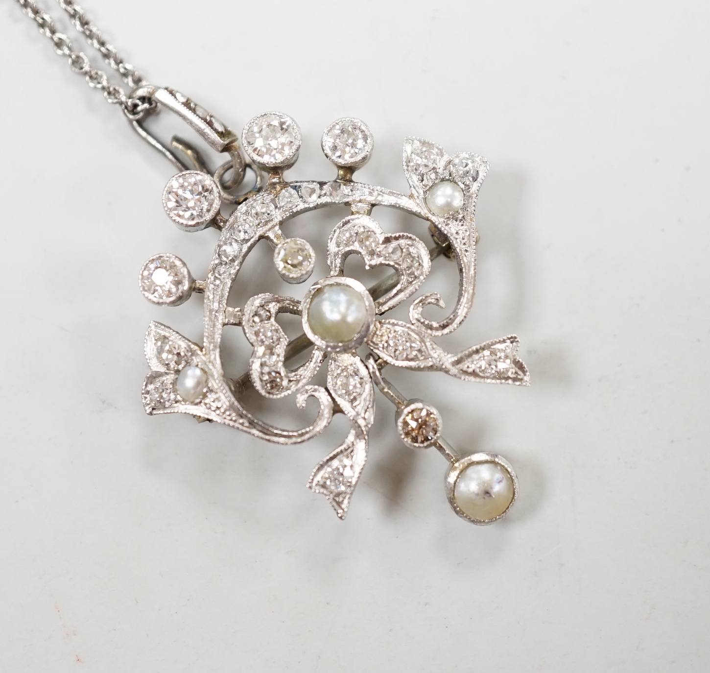 An early 20th century white metal, millegrain set diamond and split pearl cluster set drop pendant/brooch, overall 37mm, gross 5.8 grams, on a later sterling chain.